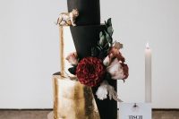 a gorgeous modern wedding cake in matte black and gold leaf, with fresh blooms, blackberries and gold figurines
