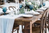 a light blue fabric table runner, blue glasses and blooms create a frozen feel at the winter wedding table