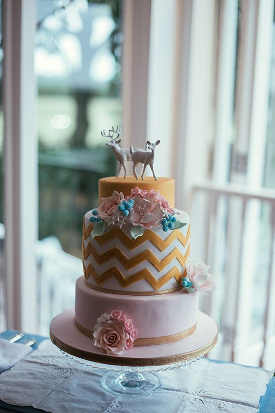 a pretty wedding cake with gold, white and gold chevron tiers, with sugar blooms and berries and deer cake toppers is an ultimate idea