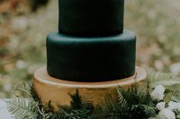 a refined modern wedding cake with matte black and a gold tier, with greenery and wildflowers on top