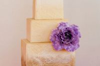 a refined patterned gold square wedding cake with a purple sugar bloom looks spectacular and wow