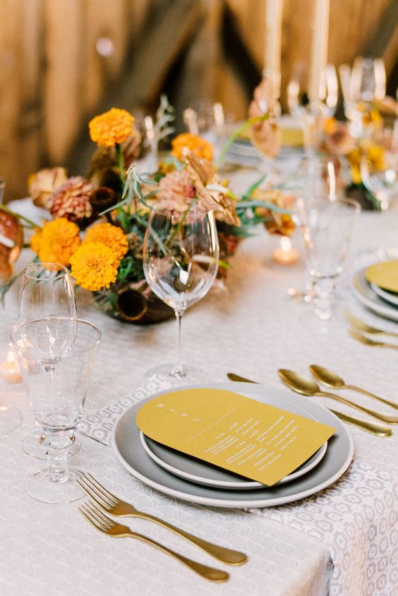 a retro-inspired wedding table setting done with mustard and grey touches, gold cutlery and bold centerpieces