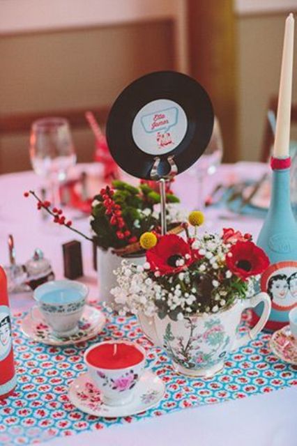 a retro wedding centerpiece with colorful candles in teacups, florals in teapots and a vinyl table name