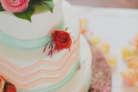 a round wedding cake with green ribbon, coral chevrons, bold roses and greenery for a summer wedding