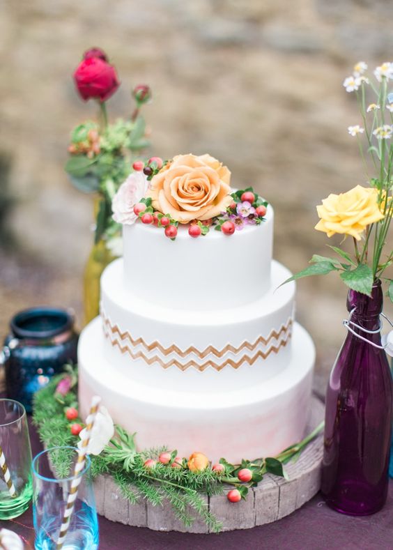 a round wedding cake with white and watercolor pink tiers, gold chevrons, fresh blooms and berries is a lovely idea for a wedding