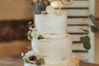 a semi naked wedding cake with white blooms and greenery, thistles, wood slices and burlap is a lovely idea for a rustic wedding
