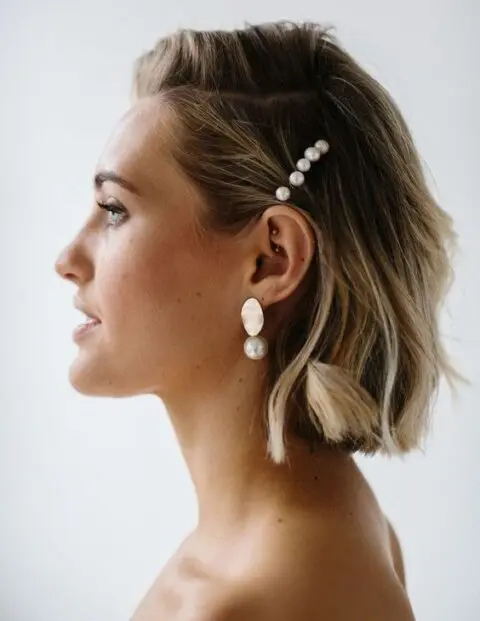 a short wavy bob with balayage and with a pearl hair barrette and matching earrings