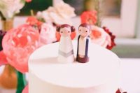 a sleek white buttercream wedding cake topped with wooden dolls showing famous Star Wars characters is a cool idea for a geeky wedding