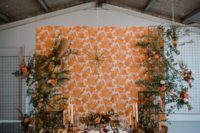 a stylish 70s inspired tablescape with a mustard tablecloth, yellow candles, florals and greenery plus a printed wallpaper backdrop