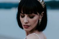 a stylish black bob with fringe and a gold and crystal crown plus matching gold earrings for a bold modern bridal look