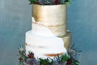 a stylish naked and gold leaf wedding cake with greenery and thistles is a bold trendy dessert