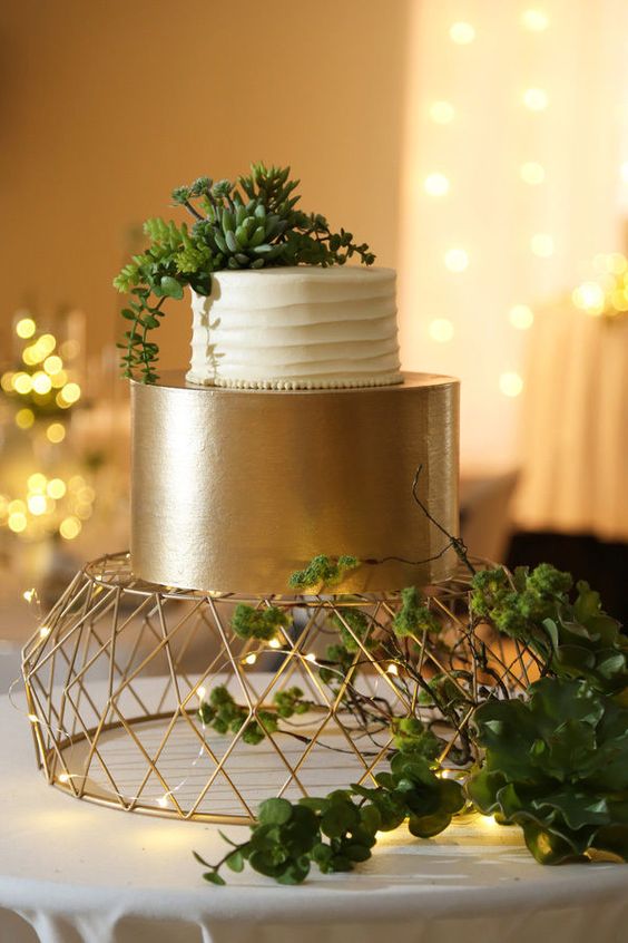 a stylish wedding cake with a white textural tier and a shiny gold one, with succulents on top is wow