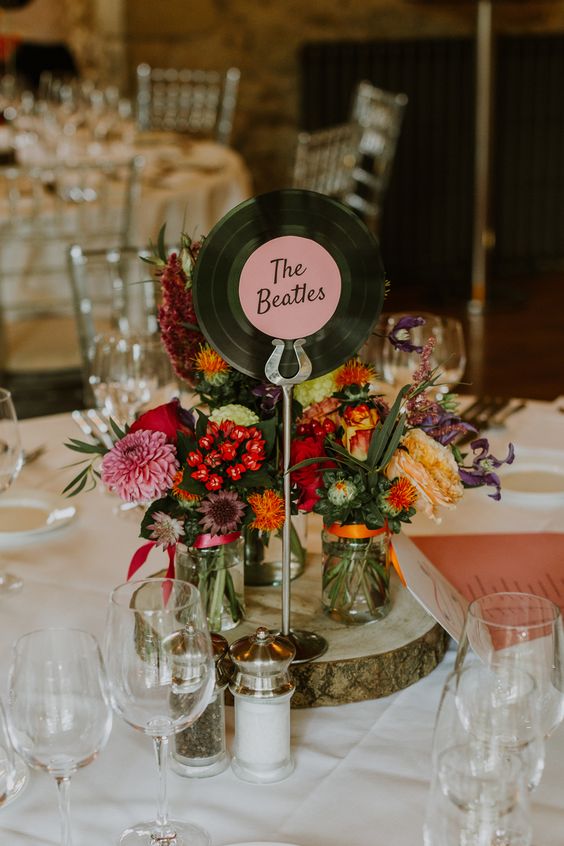 a stylish wedding centerpiece with a wood slice, colorful blooms, a vinyl table name for a retro meets rustic wedding
