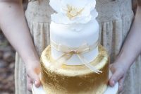 a stylish white and gold leaf wedding cake with a ribbon bow and a white sugar flower on top