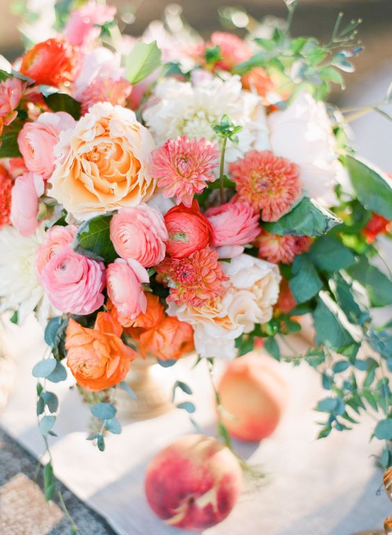 a warm colored wedding centerpiece in peachy, pink, white and with some greenery cascading