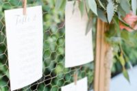 a wedding seating chart with gold frames, greenery and coral poenies looks very pretty and very fresh