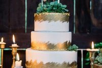 a white and gold wedding cake, with sugar succulents and olg leaf, with a gold glitter calligraphy topper