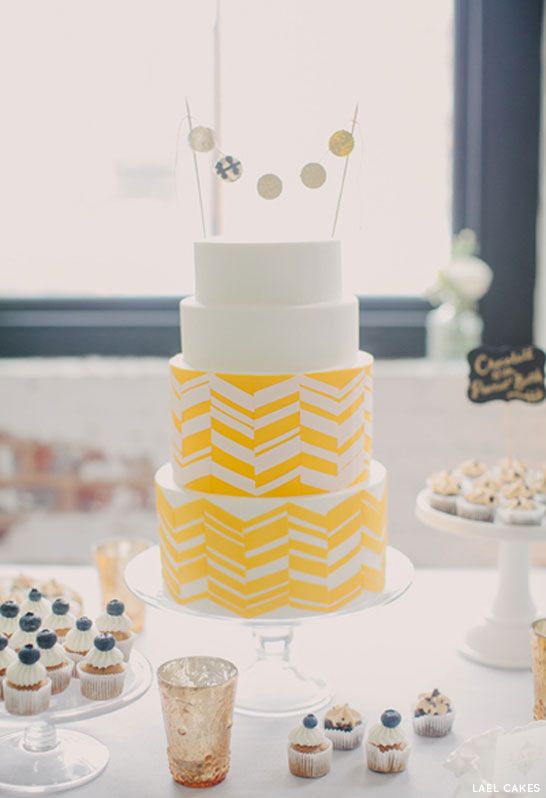 a white and yellow chevron printed wedding cake with a round banner cake topper is a chic and bold idea for a mid-century modern wedding