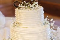 a white buttercream wedding cake with baby’s breath and a twig monogram on top is a cool idea for a rustic wedding