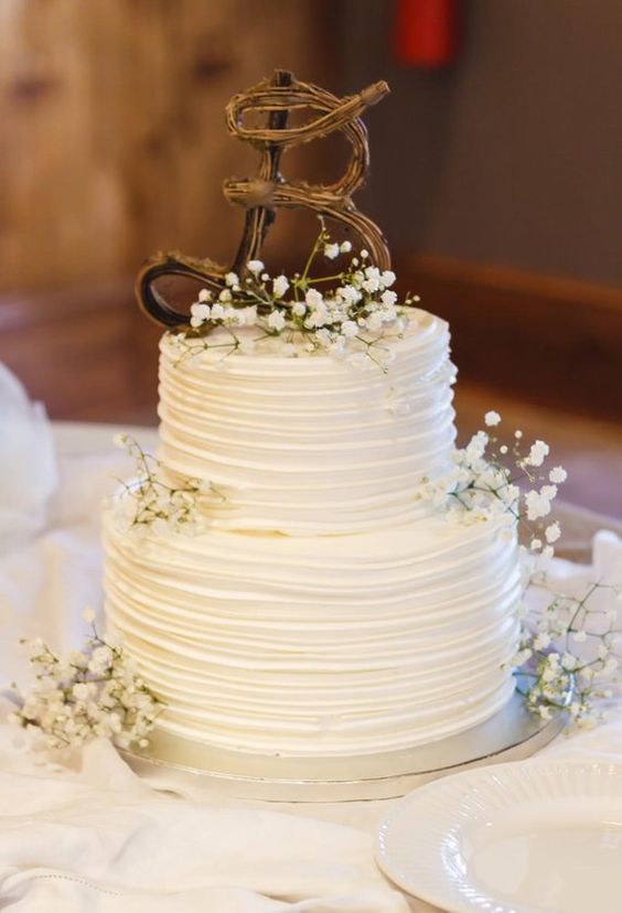 a white buttercream wedding cake with baby's breath and a twig monogram on top is a cool idea for a rustic wedding