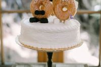 a white buttercream wedding cake with cool donut cake toppers showing a bride and a groom is a very cheerful and laid-back idea