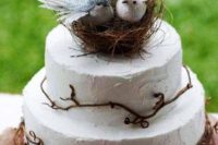 a white buttercream wedding cake with twigs and a nest with fake birds and feathers is a pretty rustic or woodland wedding cake idea