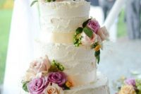 a white textural buttercream wedding cake with blush and hot pink blooms, leaves and berries plus a wire cake topper showing a couple riding a bike