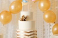 a white wedding cake with a gold chevron tier, a gilded succulent and colorful flag cake toppers for a modern wedding