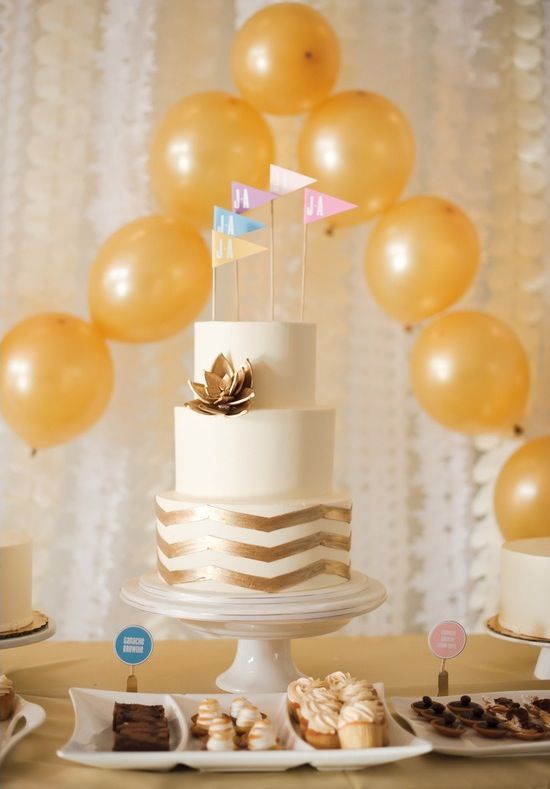 a white wedding cake with a gold chevron tier, a gilded succulent and colorful flag cake toppers for a modern wedding