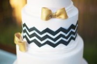 a white wedding cake with black chevron decor and gold bows is a lovely idea for a modern wedding with a touch of glam