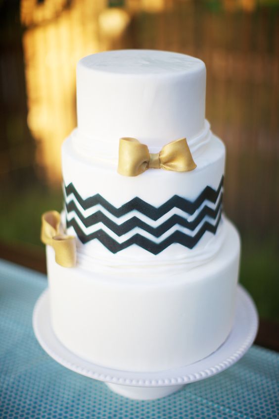 a white wedding cake with black chevron decor and gold bows is a lovely idea for a modern wedding with a touch of glam