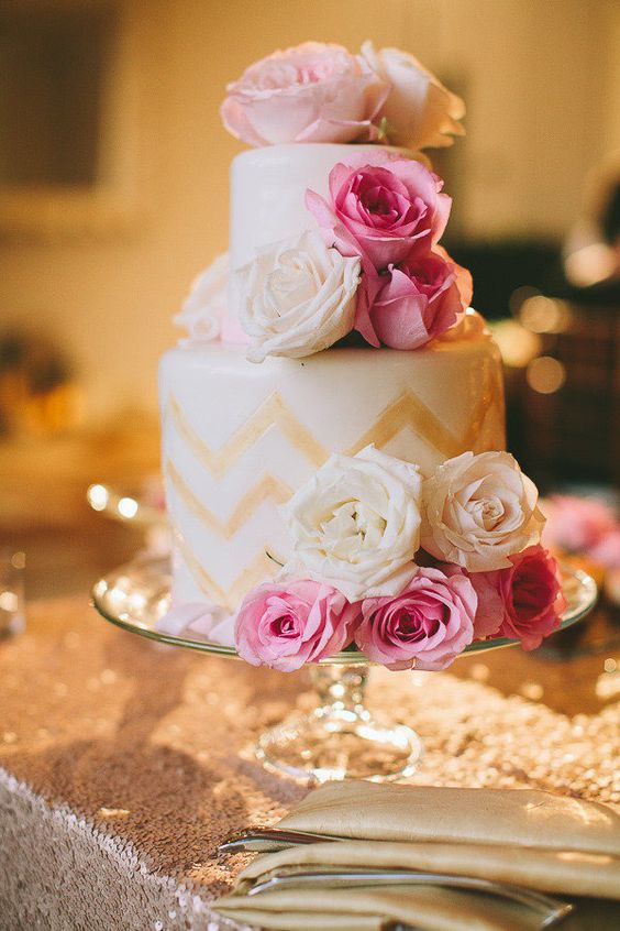 a white wedding cake with gold chevron decor, with pink and white roses is a beautiful dessert for a glam wedding