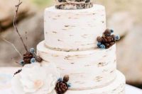 a woodland wedding cake imitating birch bark, with pinecones, faux berrites, twigs and a silk flower plus a cake topper of wood slices is cool