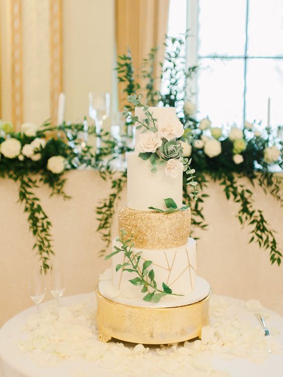 an ethereal wedding cake with white, a geometric gold and white and a gold polka dot tier, white blooms and greenery