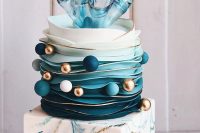 an outstanding wedding cake with a blue and gold marble cube tier, an ombre buttercream tier, blue, white and gold balls, a fantastic sheer splash cake topper