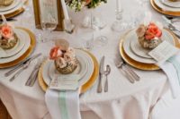 coral, peach and gold wedding tablescape with floral arrangements, white candles and white napkins with mint ribbons