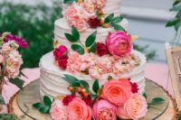 a beautiful wedding cake with pink, red and blush blooms, greenery, berries and a gold and elegant heart topper