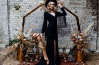 a black A-line boho wedding dress with a depe neckline, fringe sleeves and a train plus a slit, silver boots and a black hat