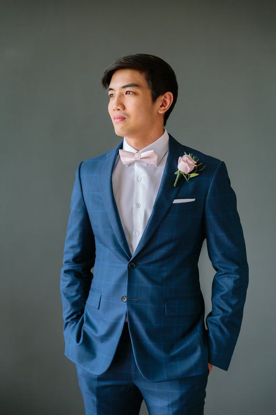 a blue plaid suit, a white shirt, a pink bow tie and a pink rose boutonniere for a chic and romantic look