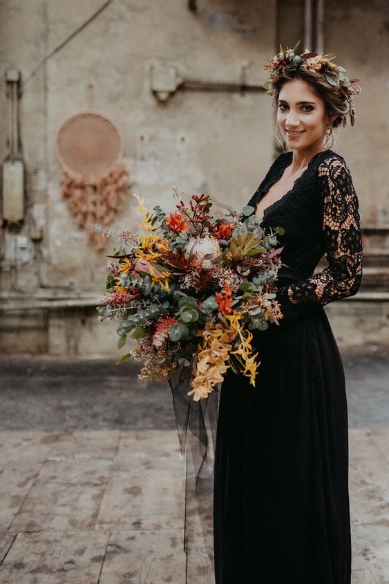 a boho fall bridal look with a black A-line wedding dress with a lace bodice and sleeves, a deep neckline and a plain skirt and a boho bridal crown