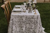 a boho lace wedding tablecloth looks incredibly chic and beautiful, tall and thin candles and greenery add chic to the table