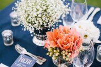 a bold wedding tablescape with a navy tablecloth, white and coral bloom centerpeices, a navy menu and a bright napkin