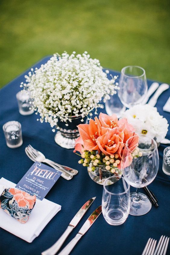a bold wedding tablescape with a navy tablecloth, white and coral bloom centerpeices, a navy menu and a bright napkin
