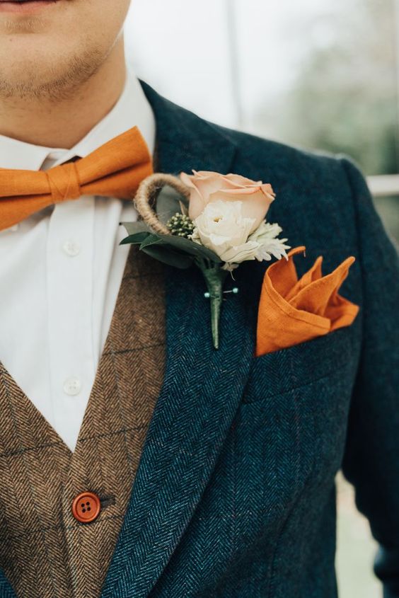 a bright fall outfit with a navy tweed suit, a brown waistcoat, an orange bow tie and handkerchief plus a neutral floral boutonniere