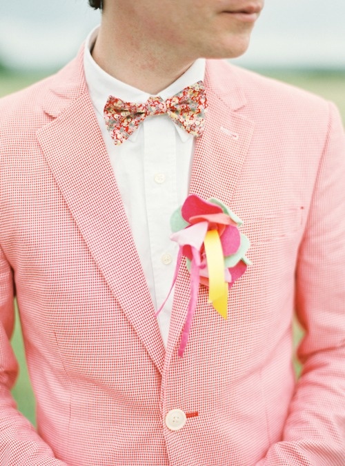 a bright pink gingham suit, a white shirt, a colorful floral bow tie and a bold fabric boutonniere for a touch of fun