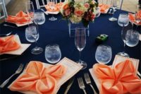 a bright wedding tablescape with a navy tablecloth, coral napkins and a coral and ivory floral wedding centerpiece