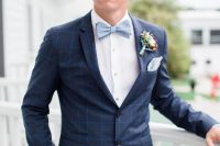 a chic navy windowpane print suit, a white shirt, a powder blue bow tie and a colorful floral boutonniere