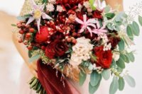 a colorful wedding bouquet of red and pink blooms, berries, foliage and long red and pink ribbons