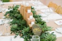 a cute natural wedding centerpiece with succulents, greenery, a large pebble, wooden stands and candles