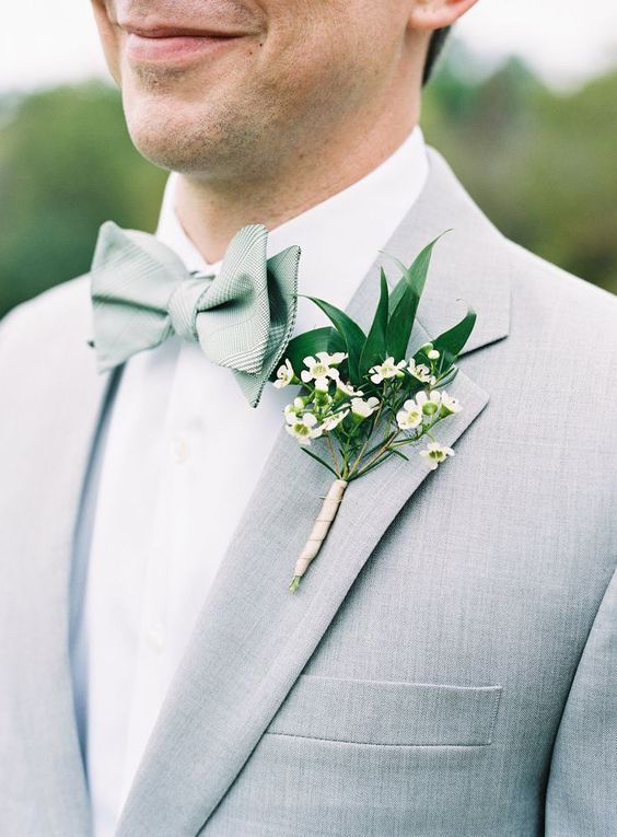 a fresh spring groom's outfit with a dove grey suit, a sage green bow tie and a greenery and neutral floral boutonniere